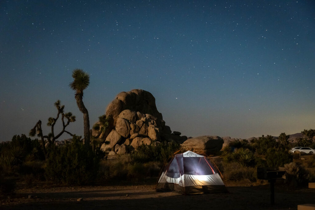 Night sky with Milky Way in Joshua Tree National Park with a lit up tent in the front
