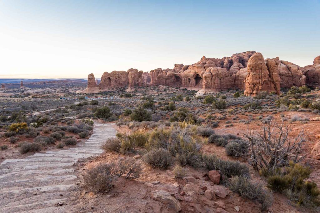 Double O Arches seen through a hiking trail surrounded by bushes post sunset