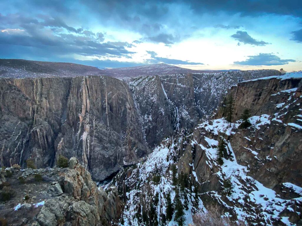 Rugged cliffs of the Black Canyon with snow and bushes in front