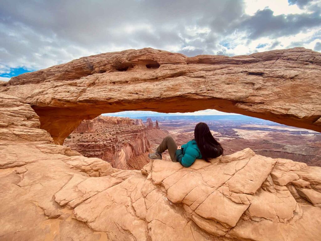 cat xu laying in front of The iconic Mesa Arch