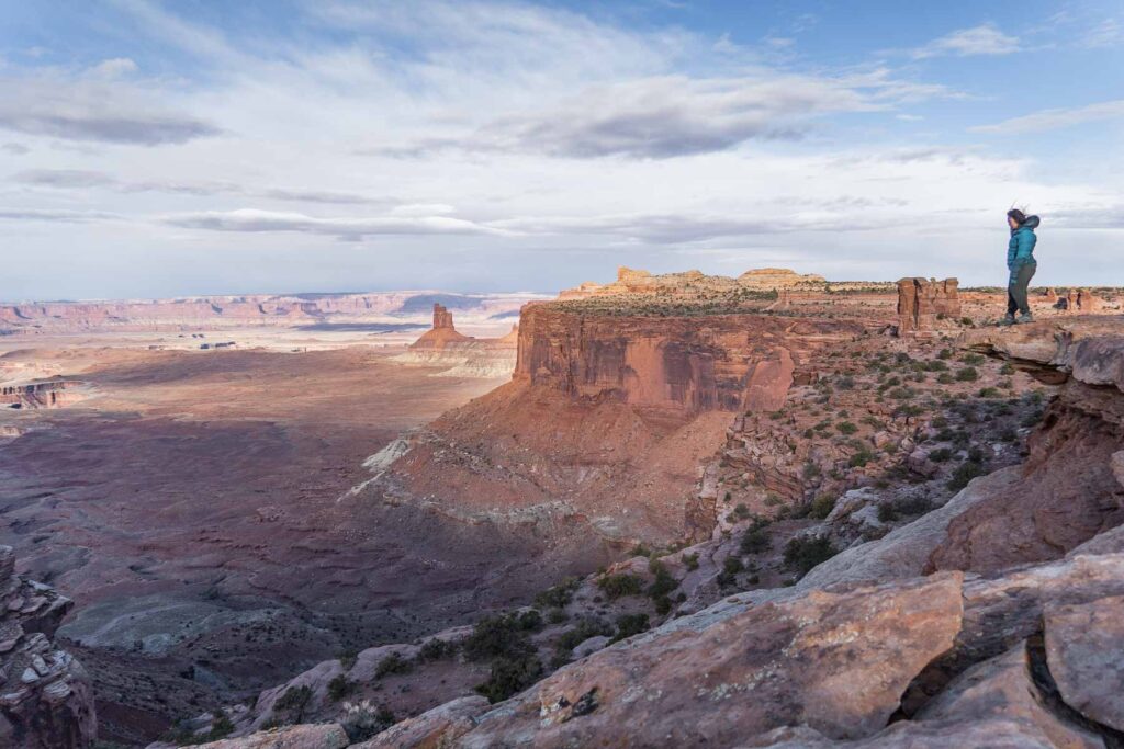 A hiker, catherine xu, standing on the edge of a cliff, overlooking the sprawling Canyonlands.