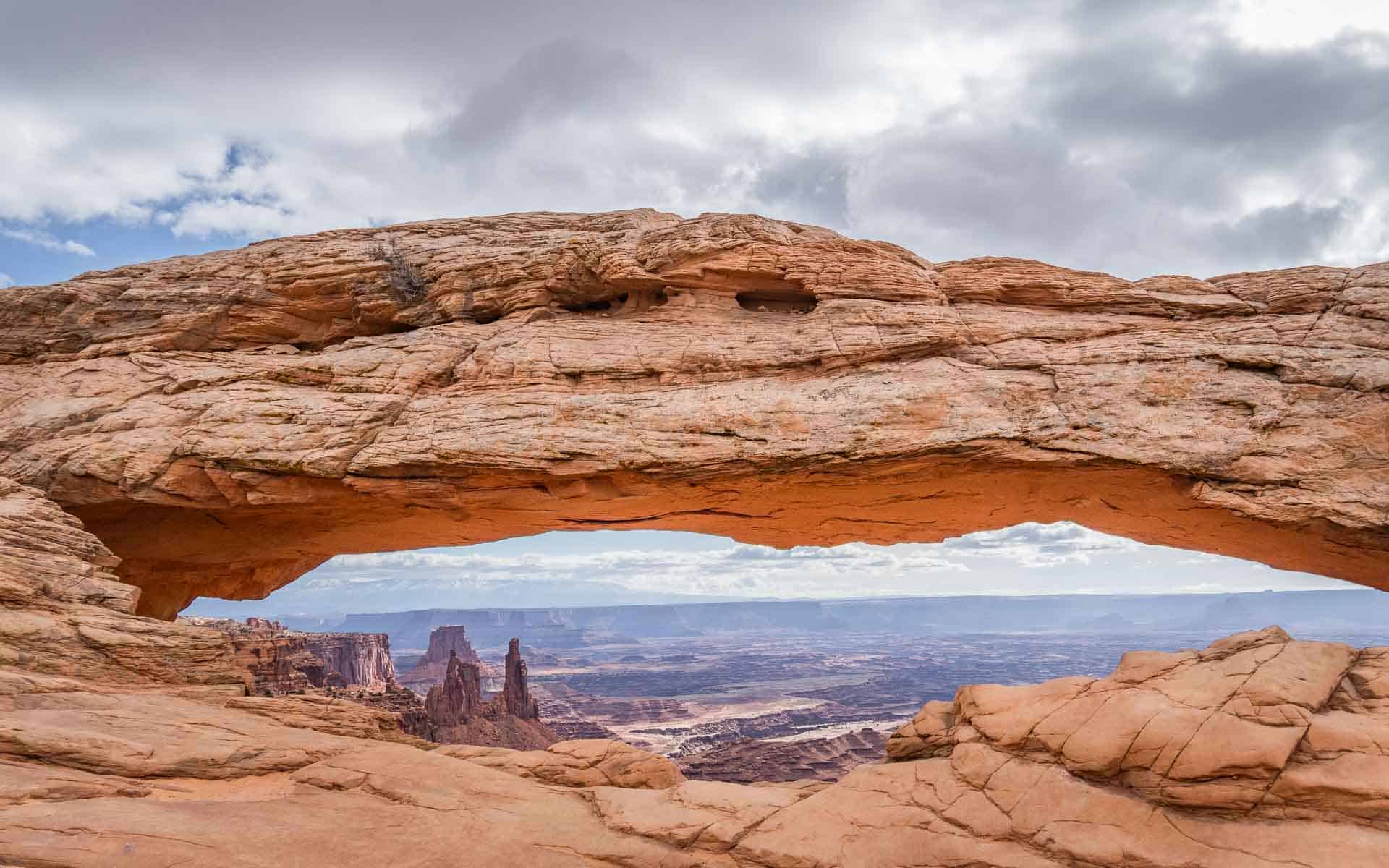 The iconic Mesa Arch, with the sun shining on the canyon and cloudy skies