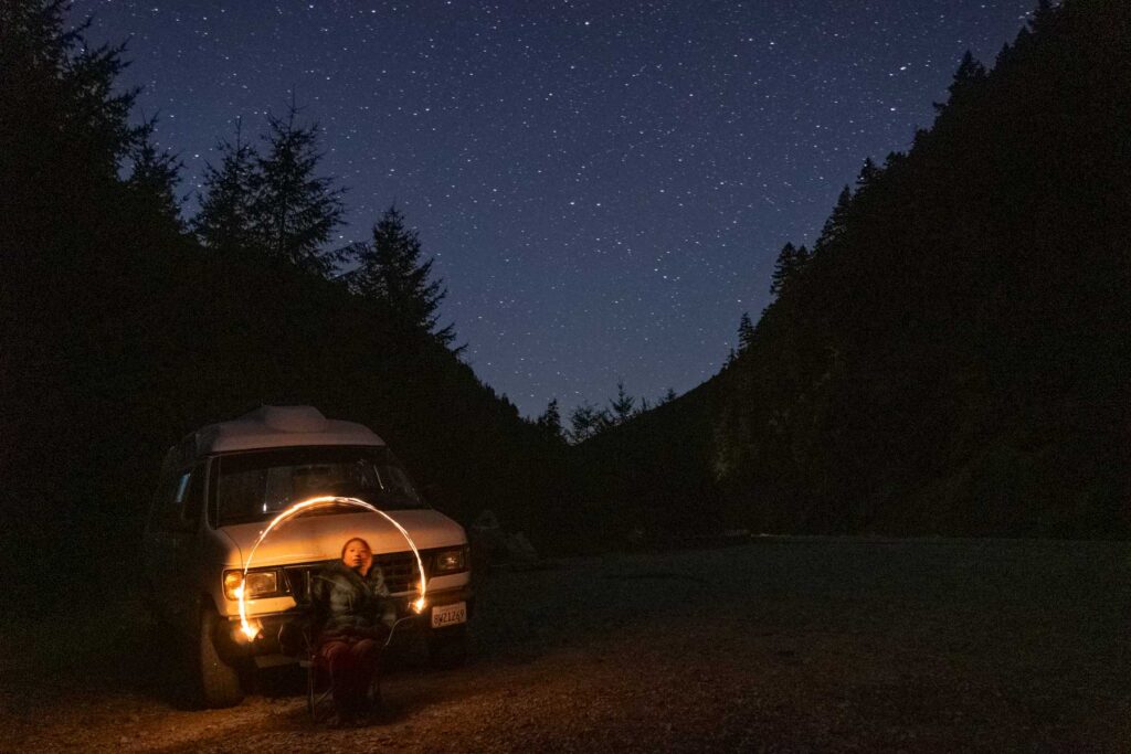 cat xu playing with a lighter sitting on front of her van on a starry night noear north cascades