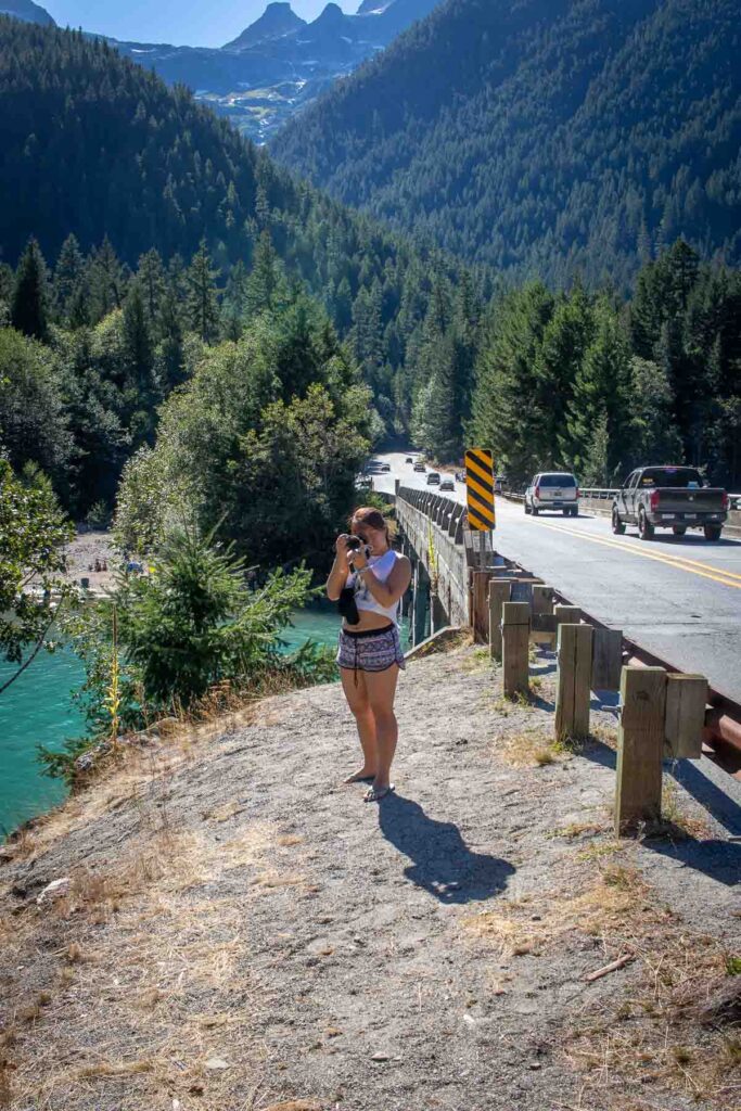 cat xu standing with a camera on the side of the highway on a day trip to the north cascades national park