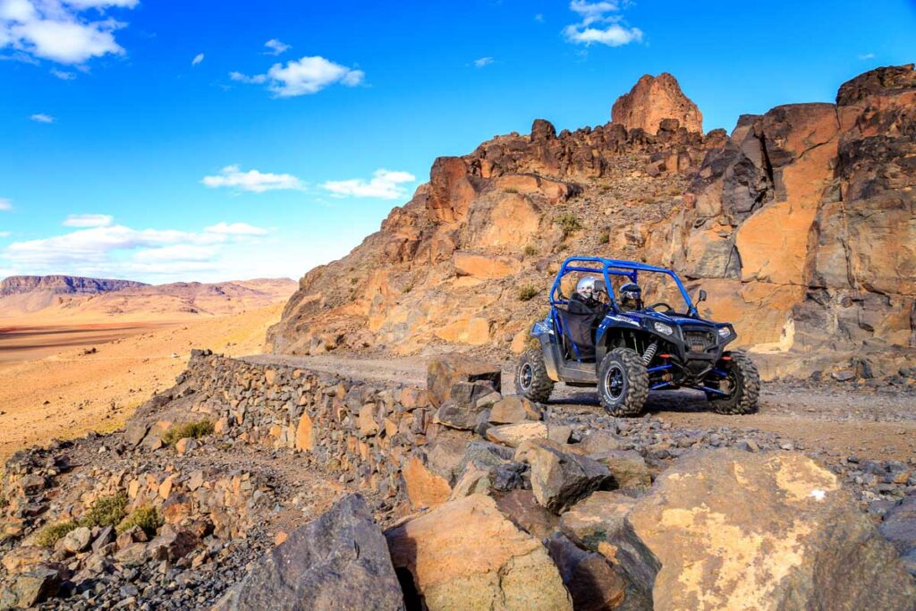 blue Polaris RZR 800 crossing a mountain road in the desert