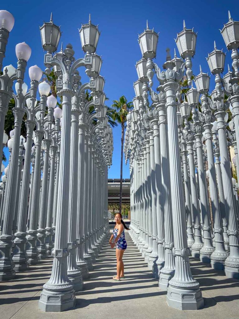Day Trip Nomad standing in the rows of the LACMA street lamps, a beautiful photo stop on a one day in los angeles itinerary
