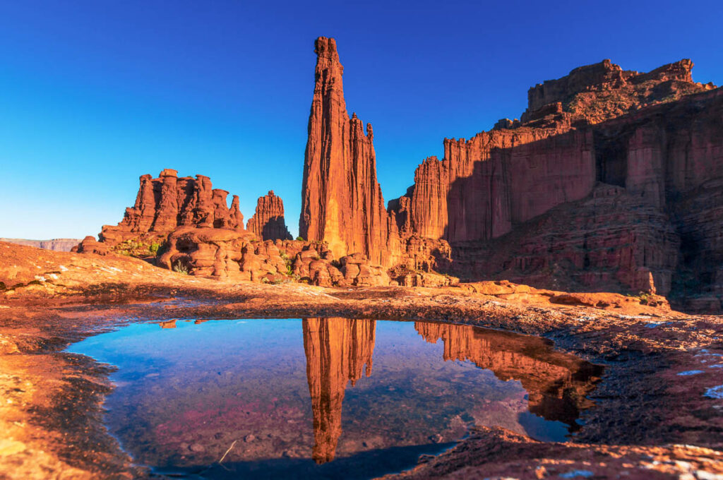 the sunset colors of Fisher Tower in Utah with a puddle of water in front