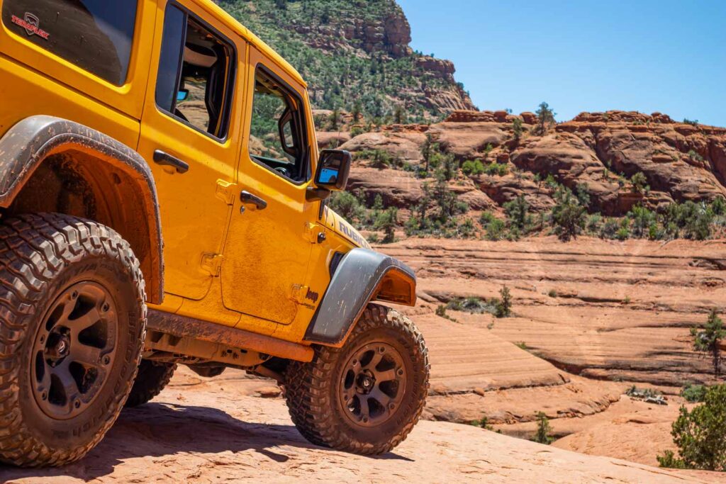 4 wheel drive jeep car on red orange rocks, desert landscape, clear blue sky, sunny spring day