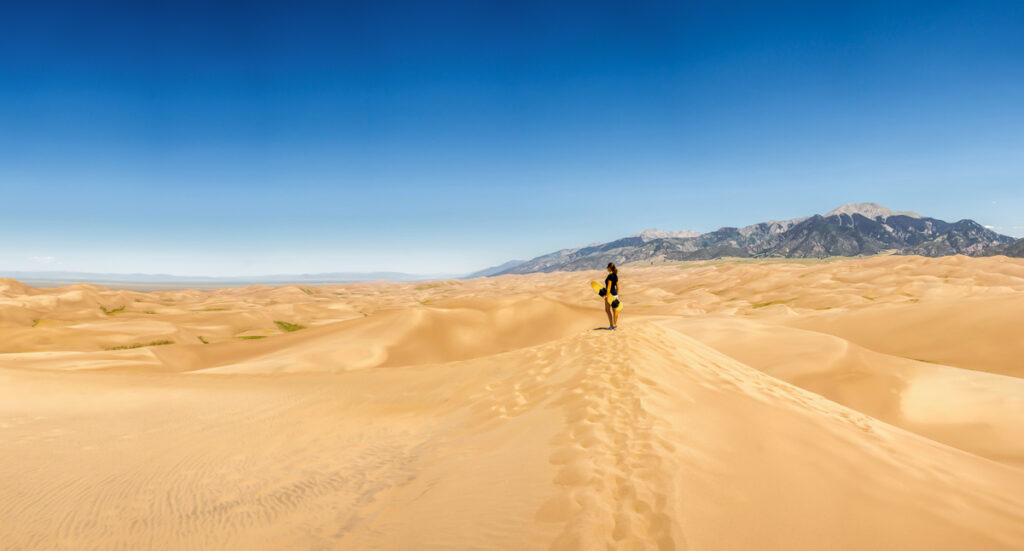 young woman with sandboard on a dune in the great sand dunes national park in colorado, united states of america