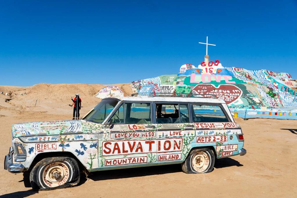 A painted car sits in front of the colorful salvation mountain in Niland, California