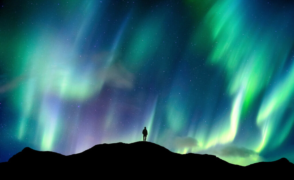 Beautiful Aurora borealis, Northern lights glowing over silhouette hiker standing on the mountain in the night sky