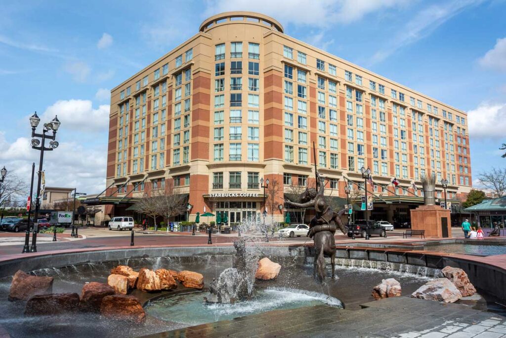 Sugar Land, Texas, United States of America.  View of Sugar Land Town Square, with fountain, sculptures, building, city traffic and people.