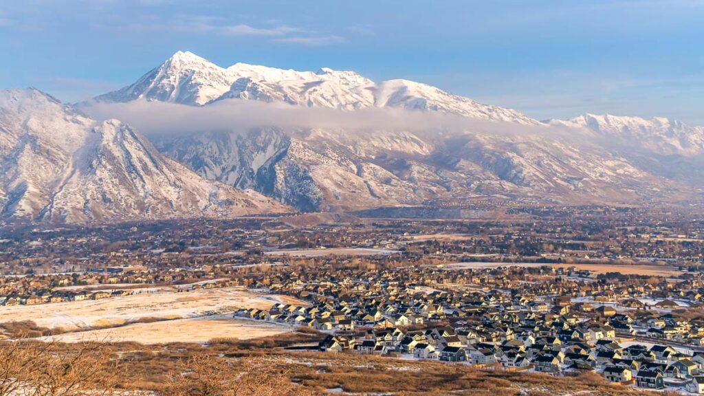 Panorama Hilly terrain and residential area against Mount Timpanogos and cloudy sky. The beautiful landscape is blanketed with fresh white snow on this cold winter day.