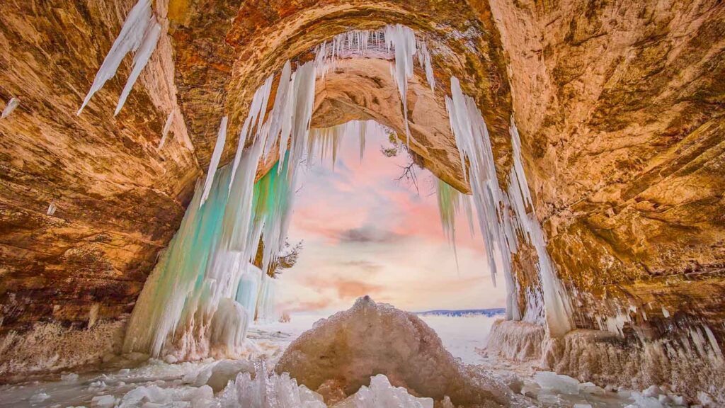 Large ice cave entrance covered in blue and green icicles and broken ice