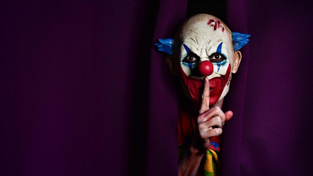 a scary evil clown peering out from a purple stage curtain, with his forefinger in front of his lips, asking for silence, with a negative space on one side