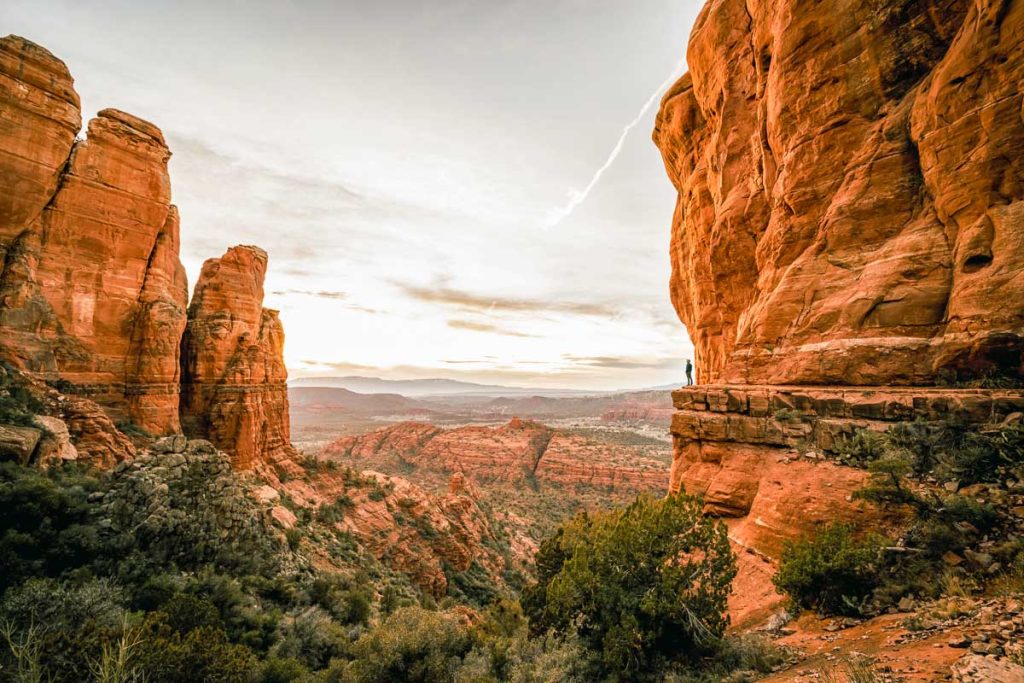 Wide angle view of man watching sunset in Sedona Arizona from Cathedral Rock Viewpoint.