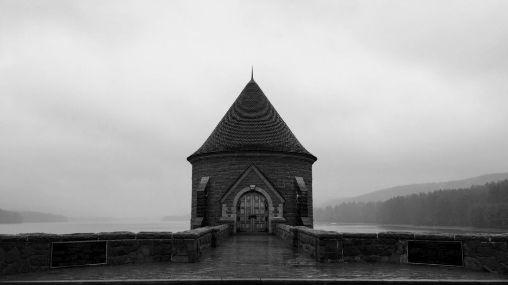 Stone tower with a steep conical roof at the end of a walkway on Saville Dam