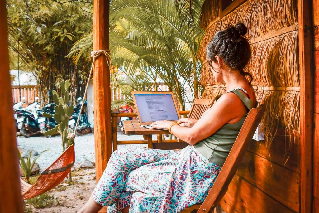 Close up young caucasian hipster woman sit use computer read news media articles, surfing, write travel blog or browse internet search or work online while traveling in southeast asia tropical islands