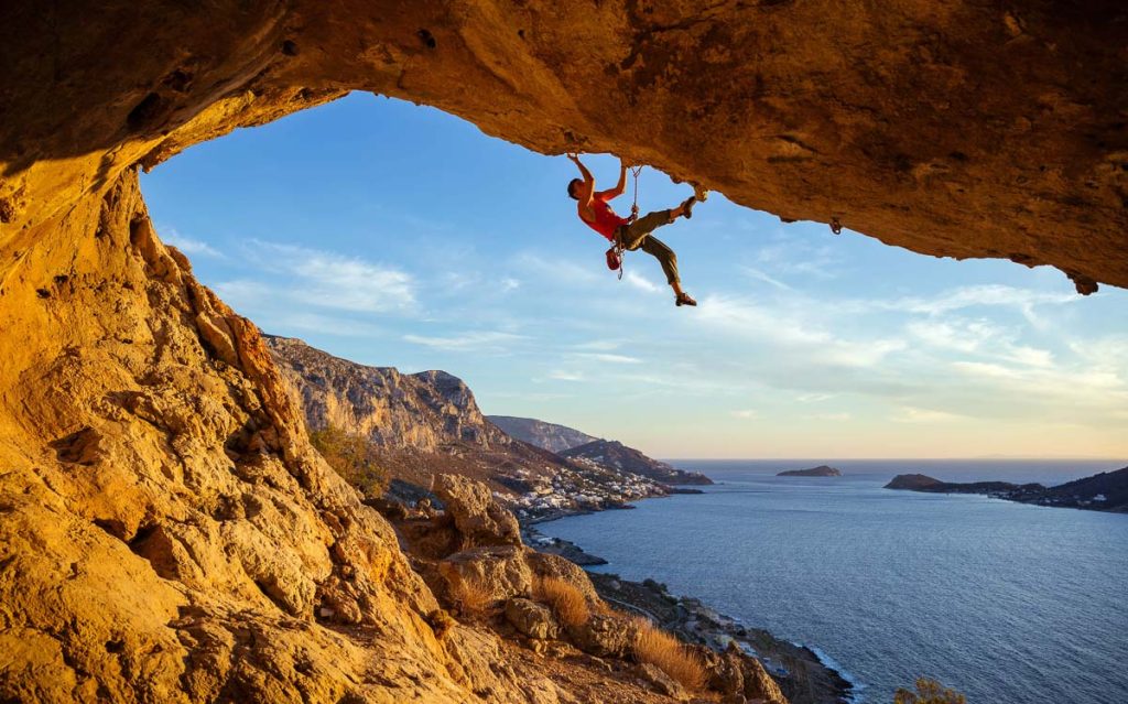 Greece, Kalymnos, male climber on overhanging rock with coastal view below