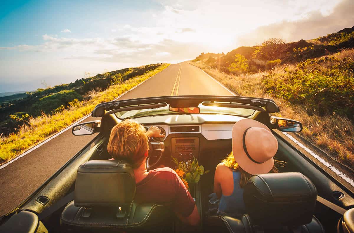 Happy Young Couple Driving Along Country Road in Convertible at Sunset