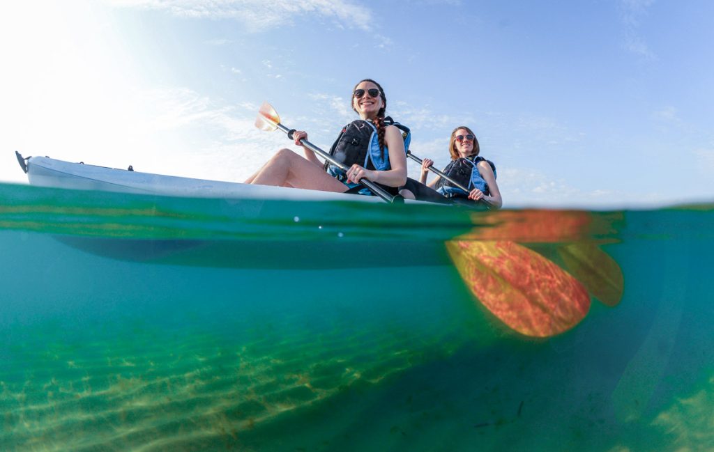 Two young women smiling in blue kayak in Atlantic Ocean off of the coast of Florida