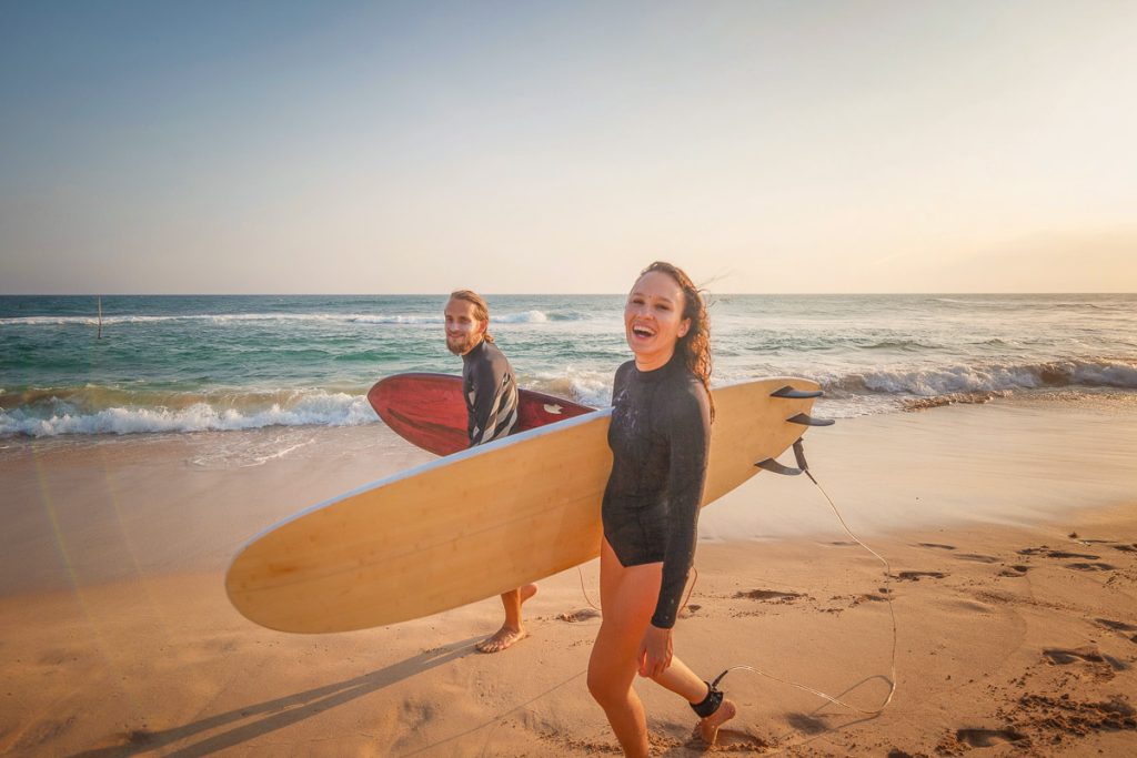 Young couple of happy smiling surfers on ocean coast, sport active lifestyle vacation travel concept