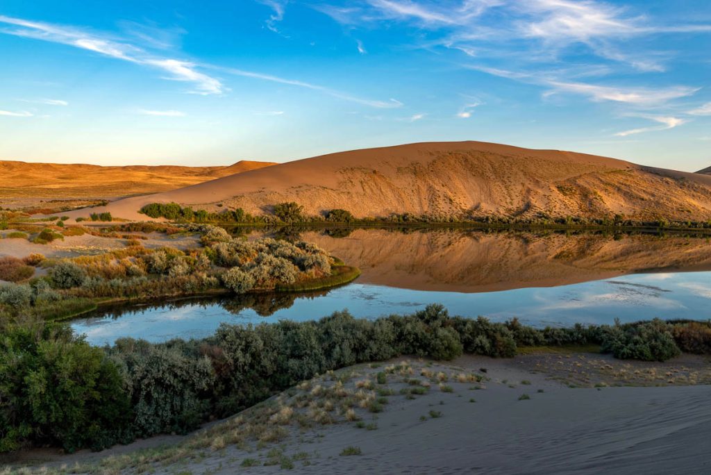 Desert oasis of water with vegetation along with blue sky and clouds at Bruneau Dunes, Idaho.