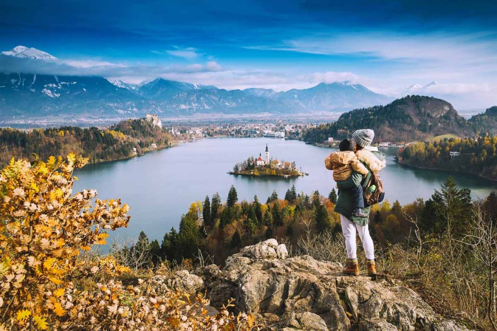 Family travel Europe. Mother with son looking on Bled Lake. Autumn or Winter in Slovenia, Europe. Top view on Island with Catholic Church in Bled Lake with Castle and Mountains in Background.