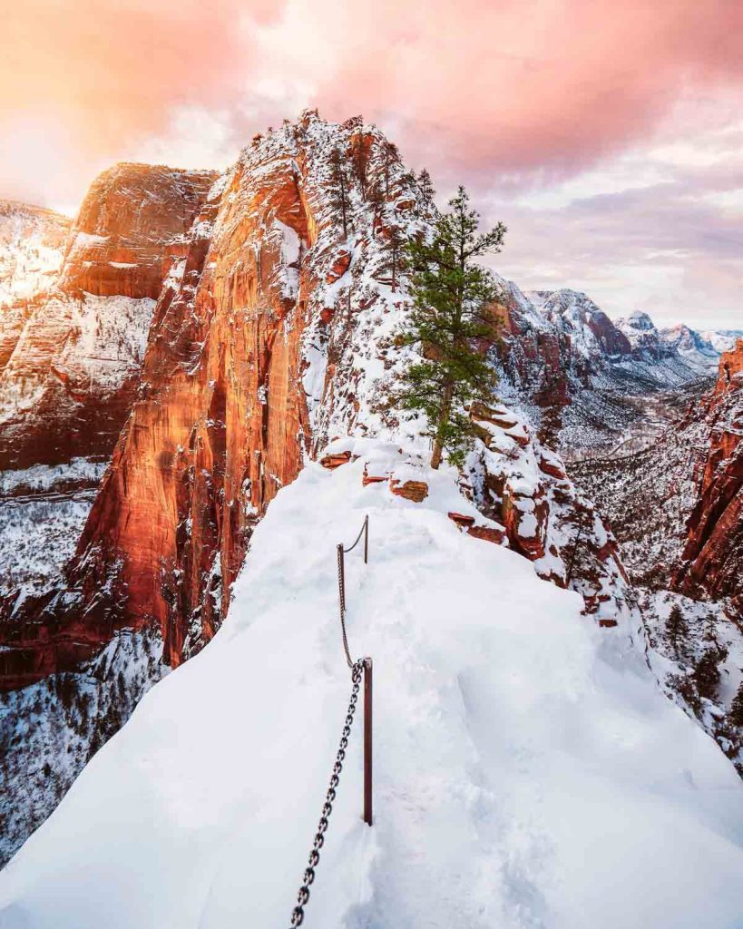 Zion National Park, snowy cliffside trail with chain railings overlooking towering red sandstone canyons at sunrise
