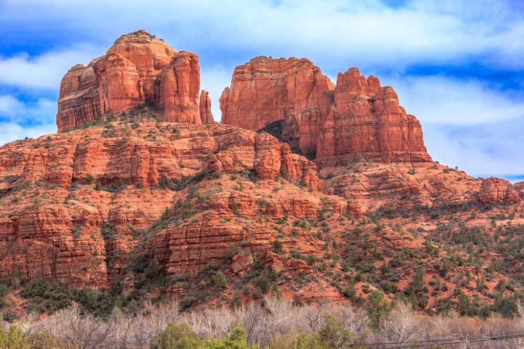 A beautiful mountain range with a mix of green and brown vegetation. The mountains are covered in red rocks, giving the scene a rugged and majestic appearance. The sky above is clear and blue