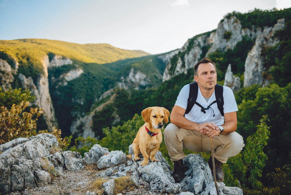 Hiker and his small yellow dog sitting on the mountain top and resting