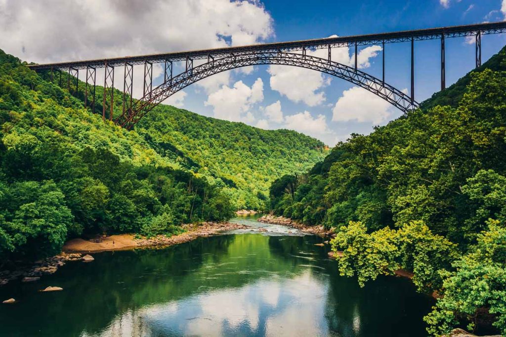 New River Gorge Bridge, West Virginia, steel arch bridge spanning the New River Gorge, framed by lush green forest and a winding river below on a bright summer day