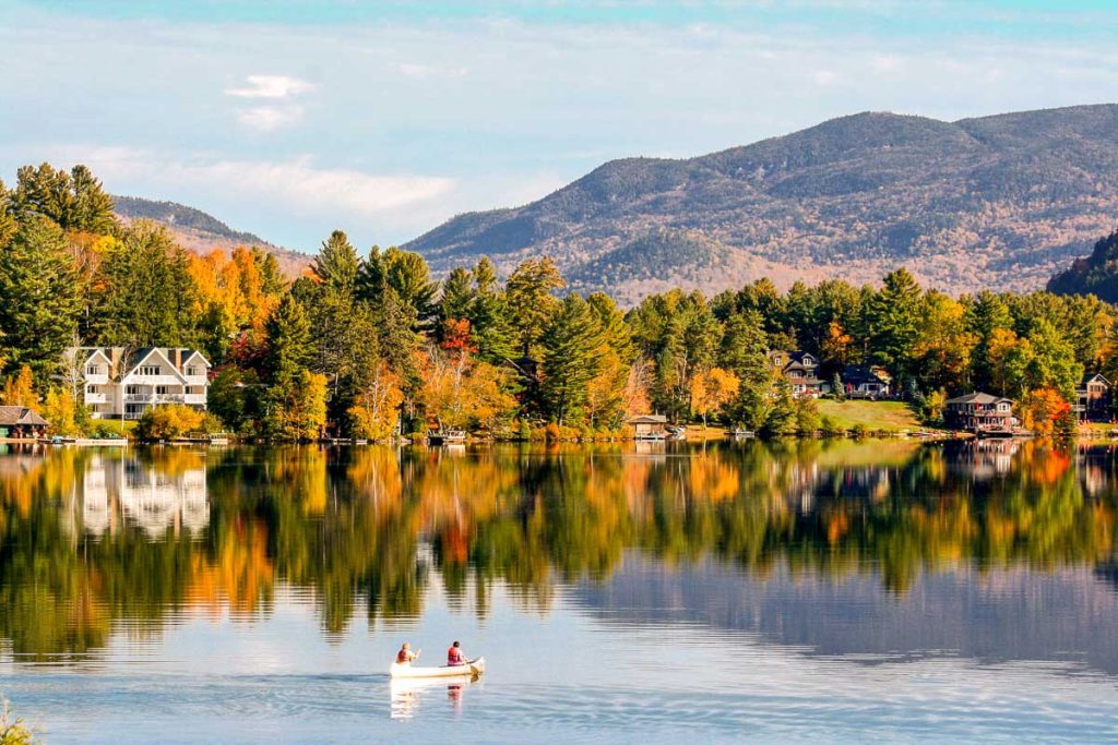 Couple canoing on Lake Placid with mountains and trees reflectin