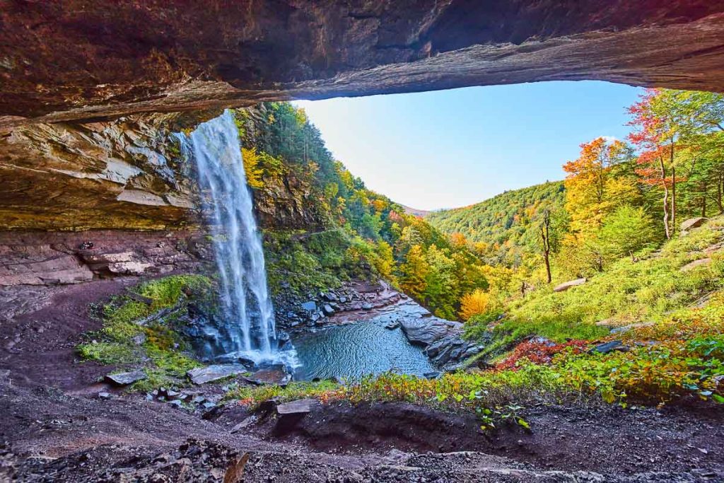 Image of Stunning view in cave behind waterfall with view of colorful fall mountains