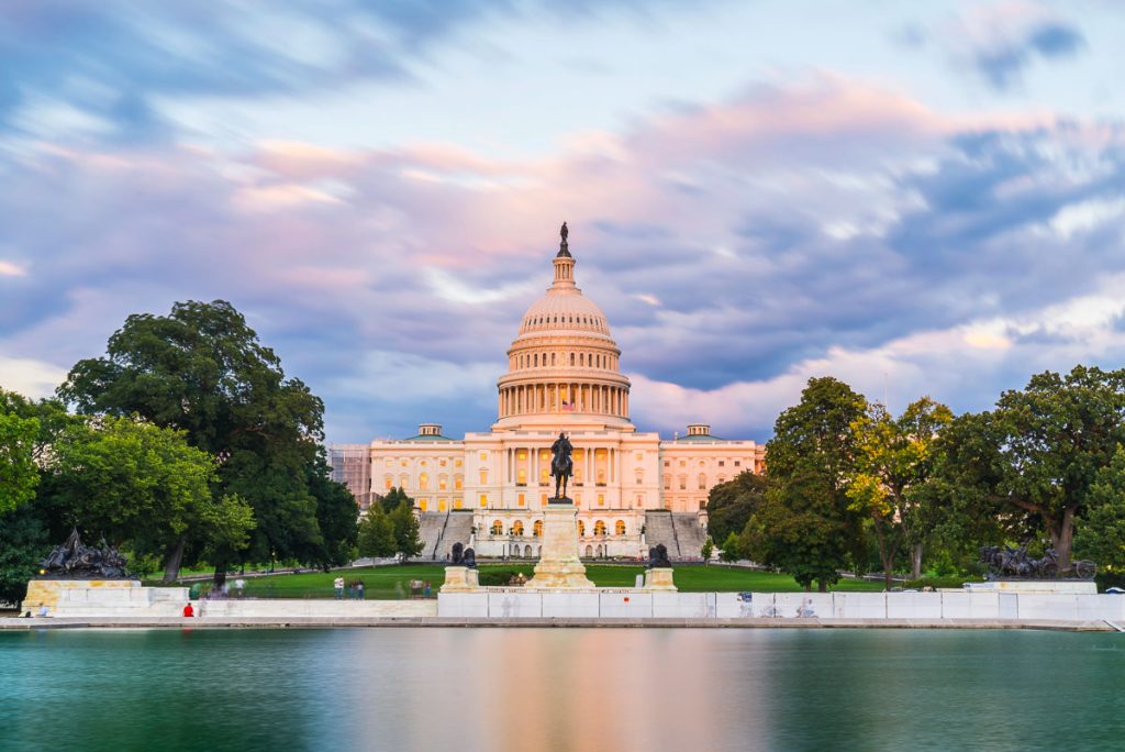 The United States Capitol building at sunset wirh reflection in water.