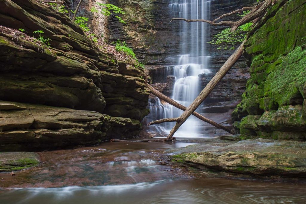 Creamy water glistens down the waterfall at Lake Falls in Matthiessen State Park, Illinois. The cascading spray provides a conducive environment to sustain the spread of soft green moss on the the limestone canyon walls.