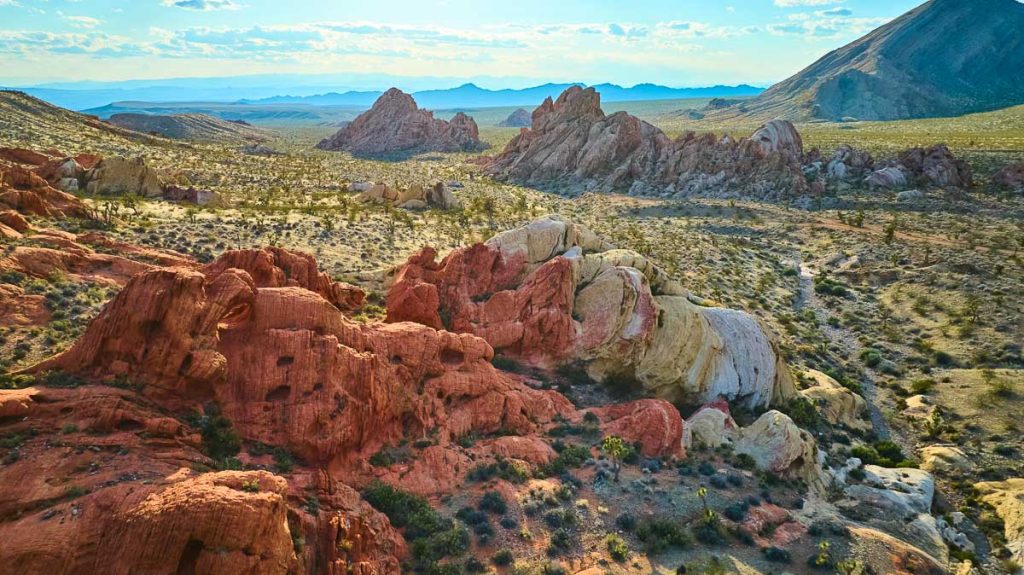 Sweeping aerial view of red and white sandstone rocks desert terrain and distant mountains in Gold Butte National Monument Nevada bathed in warm sunlight near Whitney Pocket
