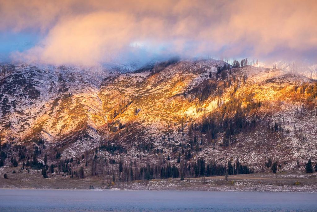 Mountain range covered by snow and cloud at sunrise of Jackson Lake, Grand Teton National Park, Wyoming, USA. Pine trees on mountain surface are dying due to climate changing.
