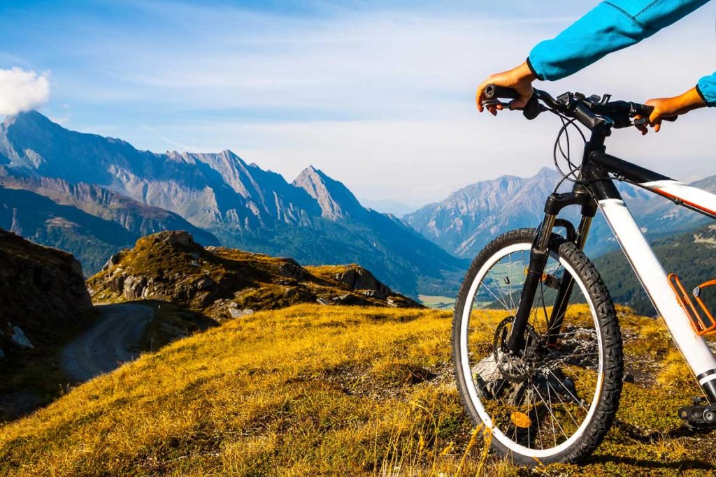 Mountain biker sports man overlooking an alpine valley with rocky peaks and golden grass